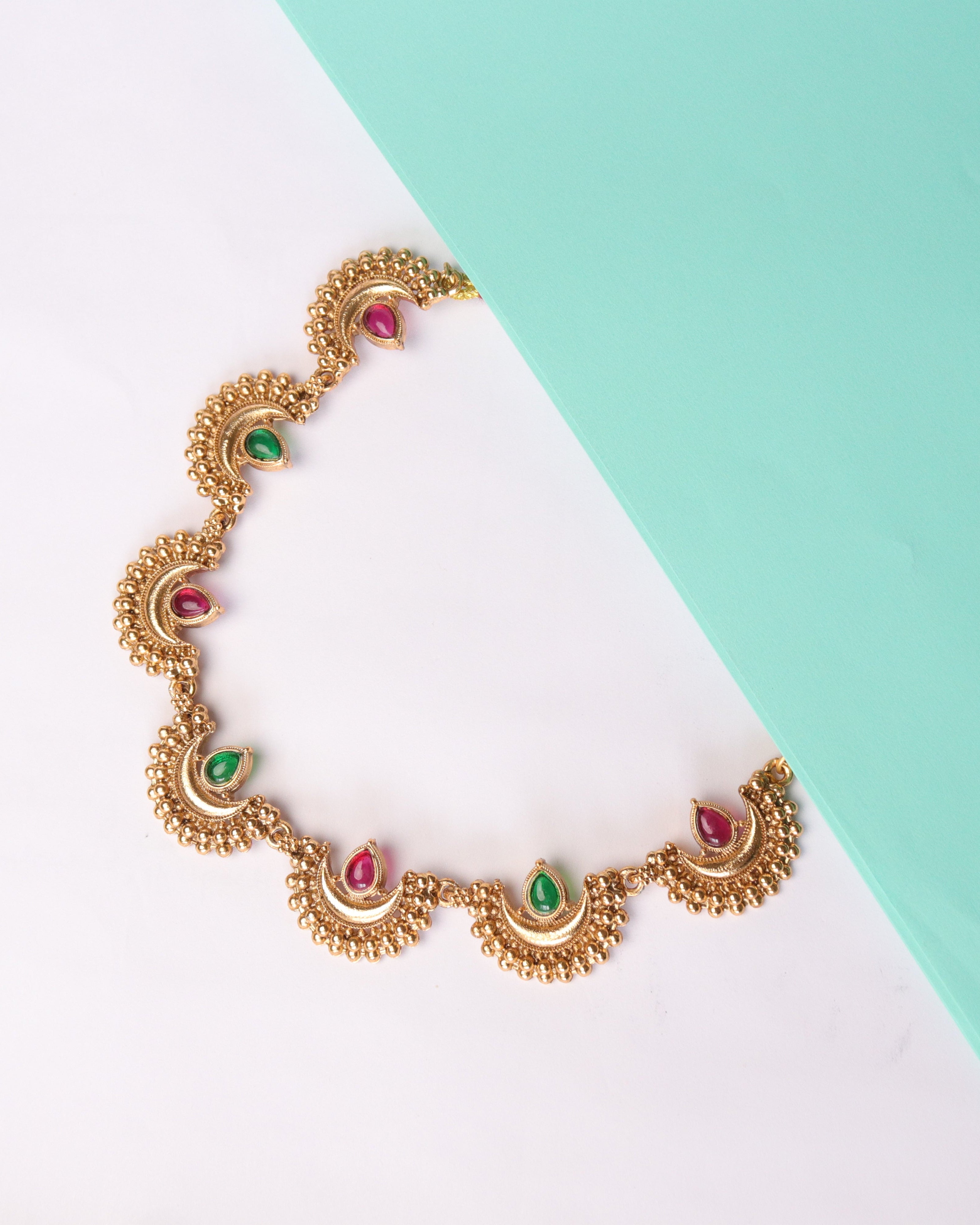 Gold necklace with colorful stones on a white and light blue background