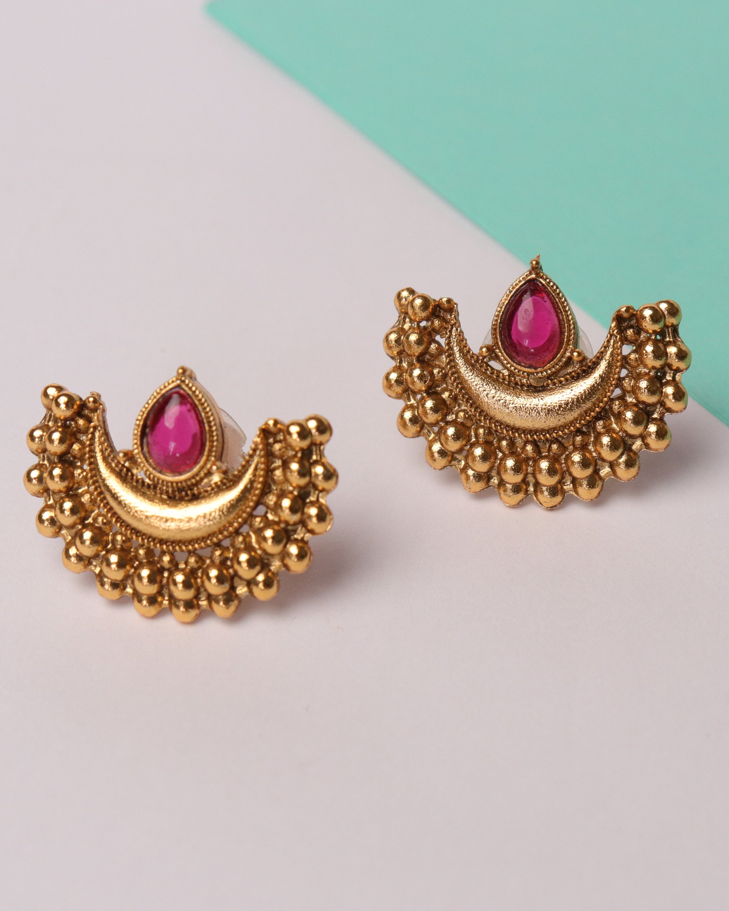 Gold earrings with pink gemstones on a two-tone background