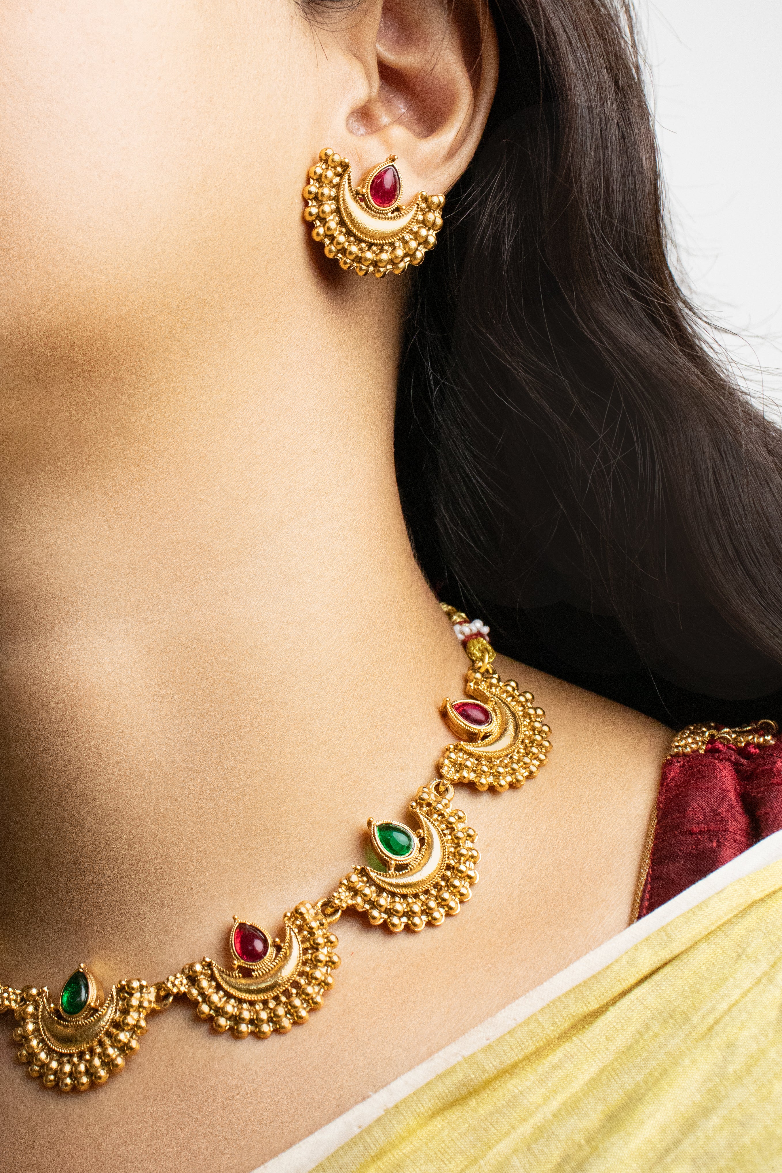 Gold necklace and earrings with red and green stones worn by a person.