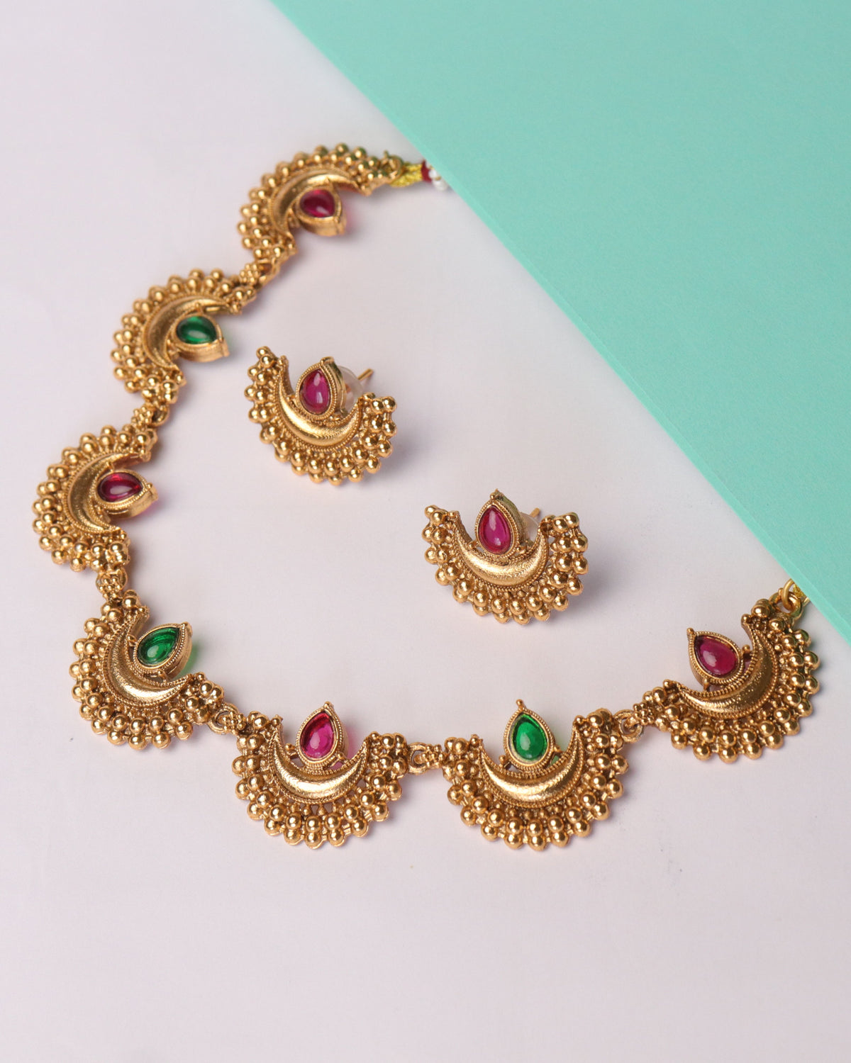 Gold necklace and earrings with gemstones on a two-tone background