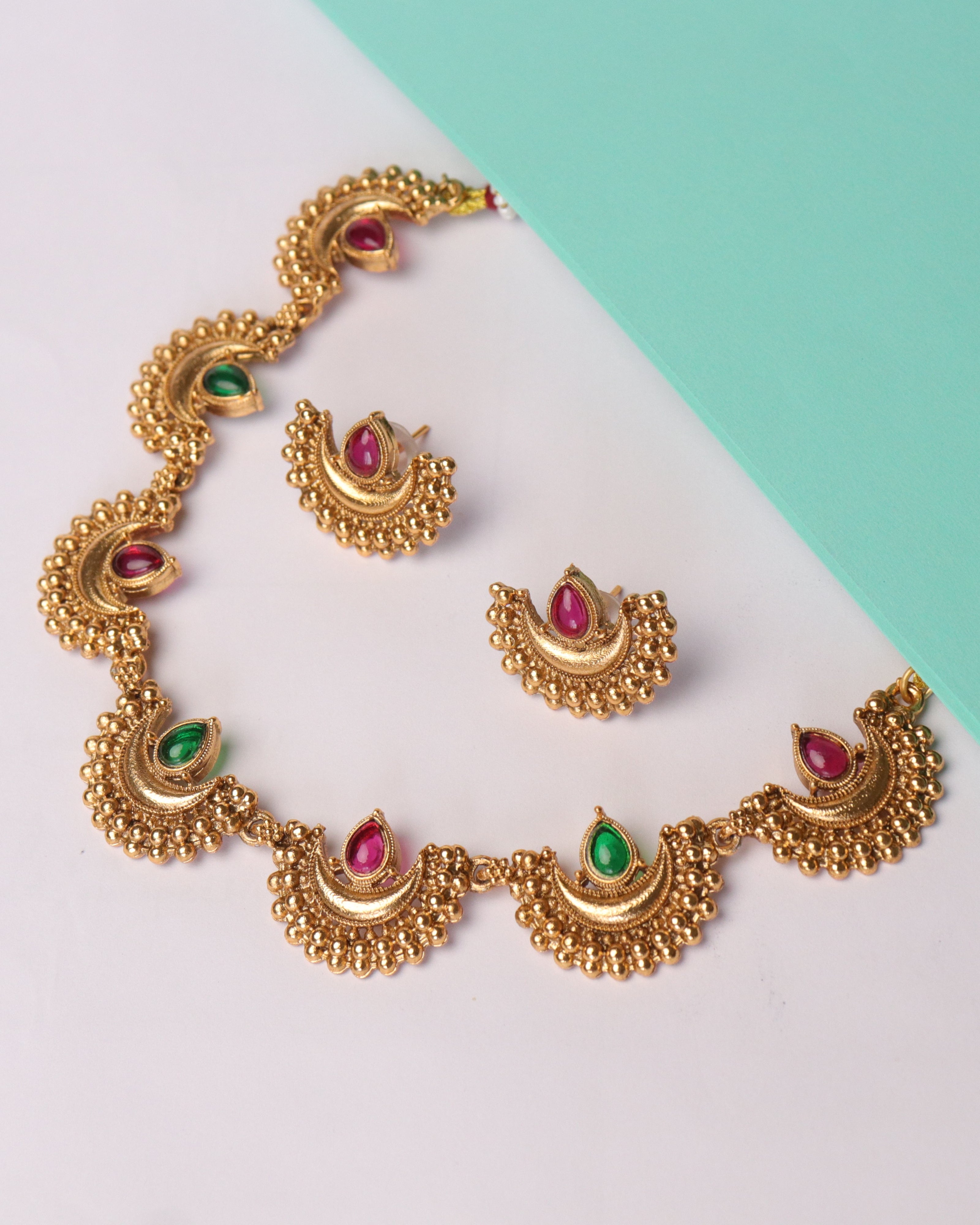Gold necklace and earrings with gemstones on a two-tone background