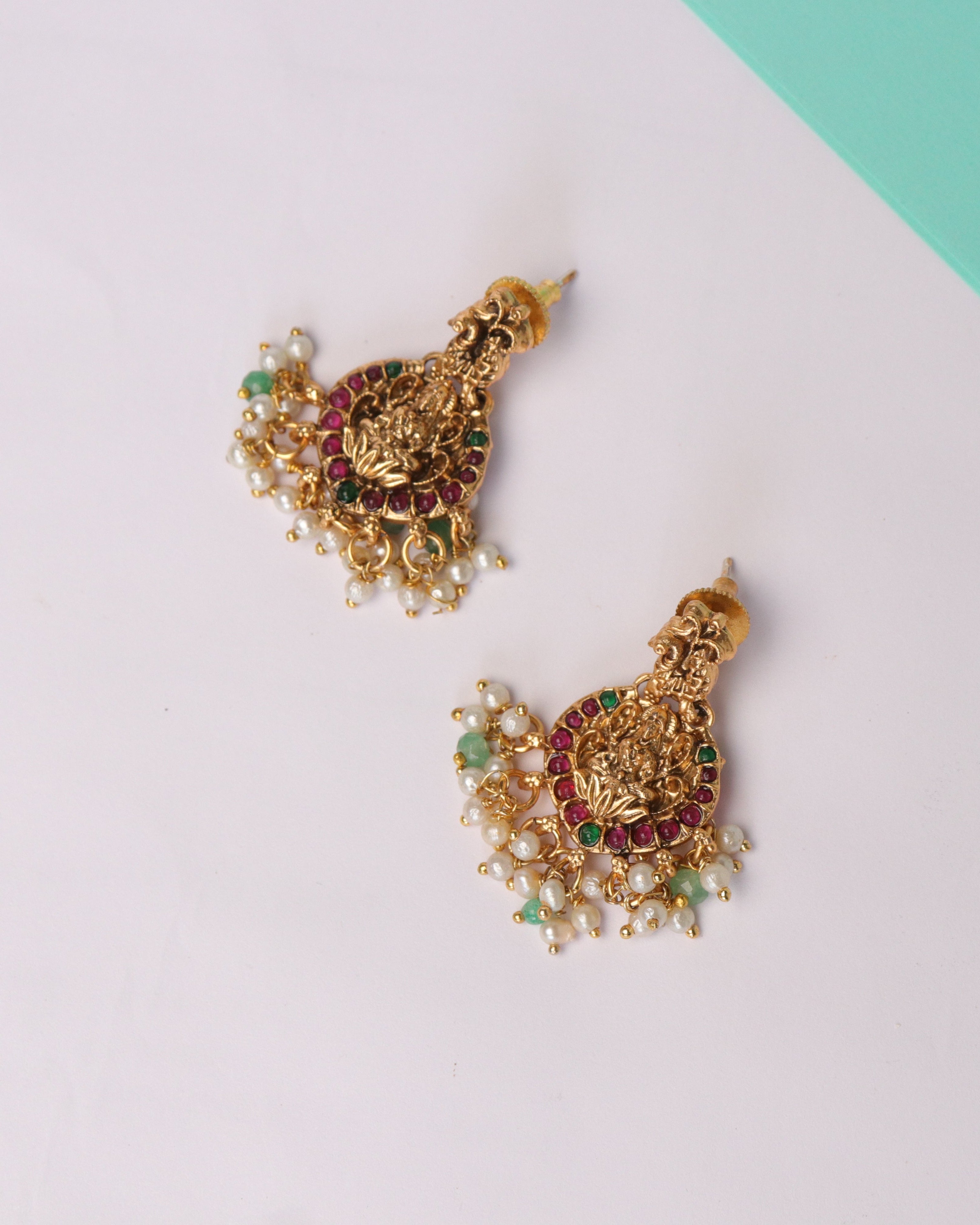 Gold earrings with gemstones on a white and green background