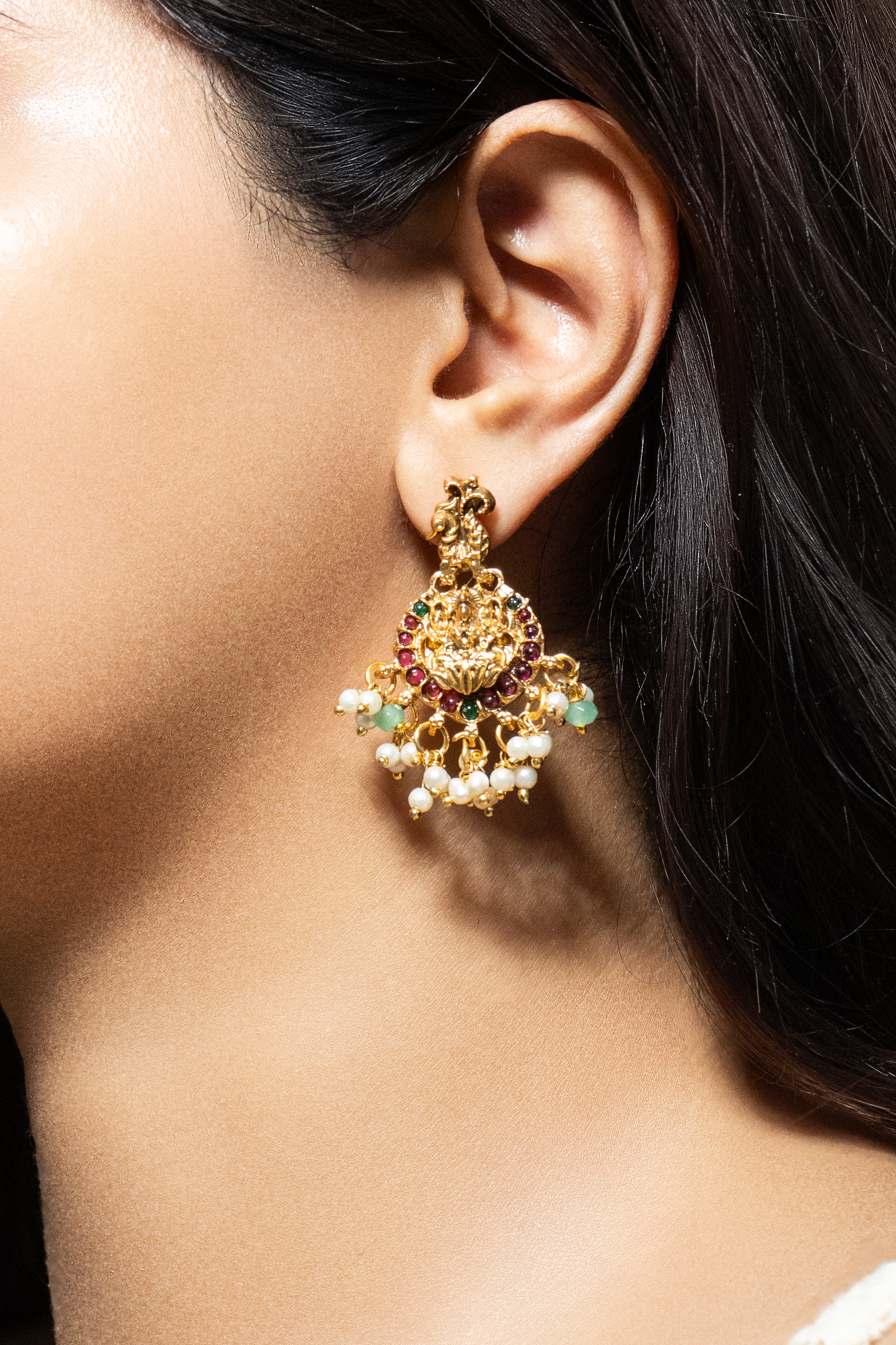 Close-up of a person wearing a gold earring with gemstones.