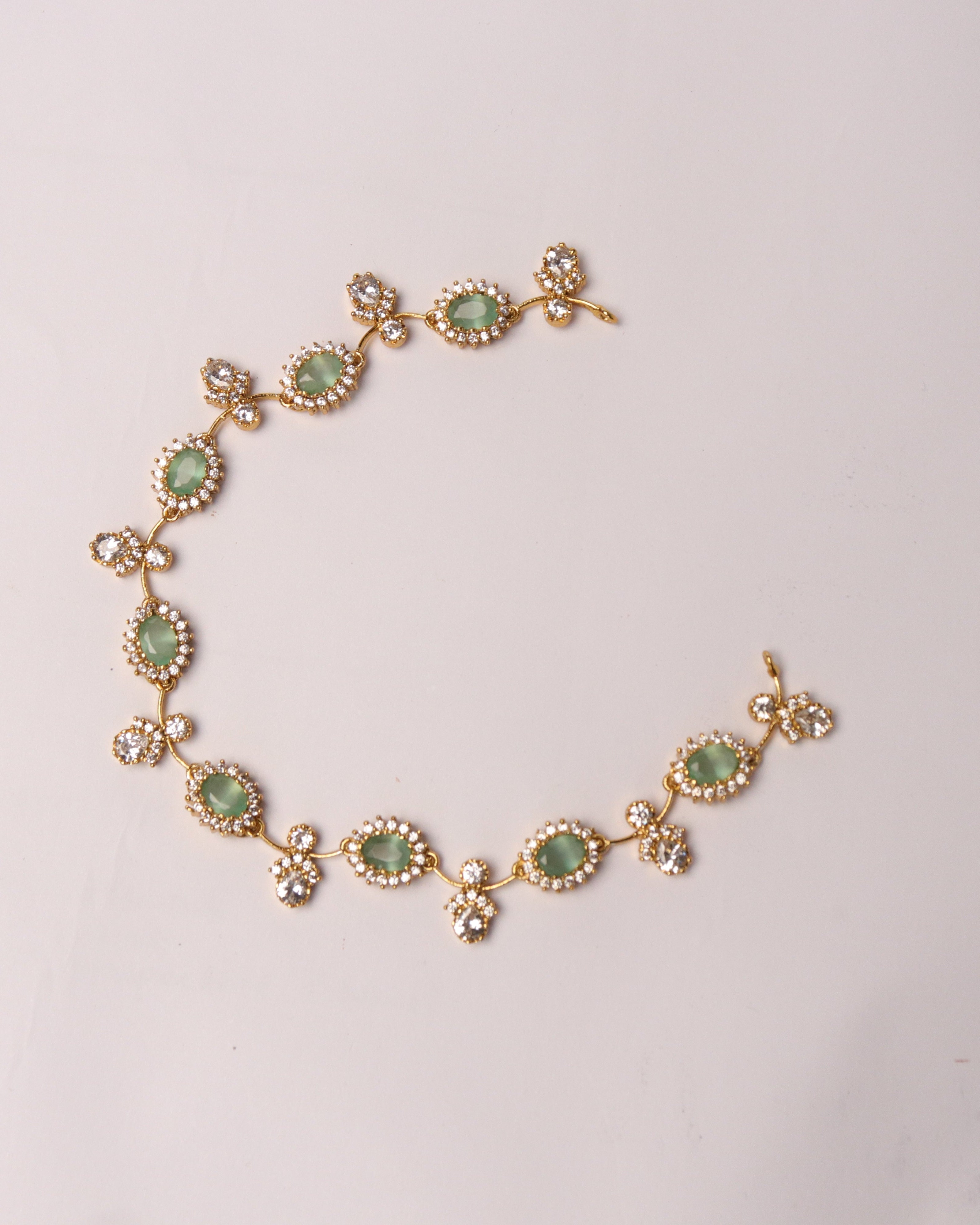 Gold bracelet with green gemstones on a light gray background