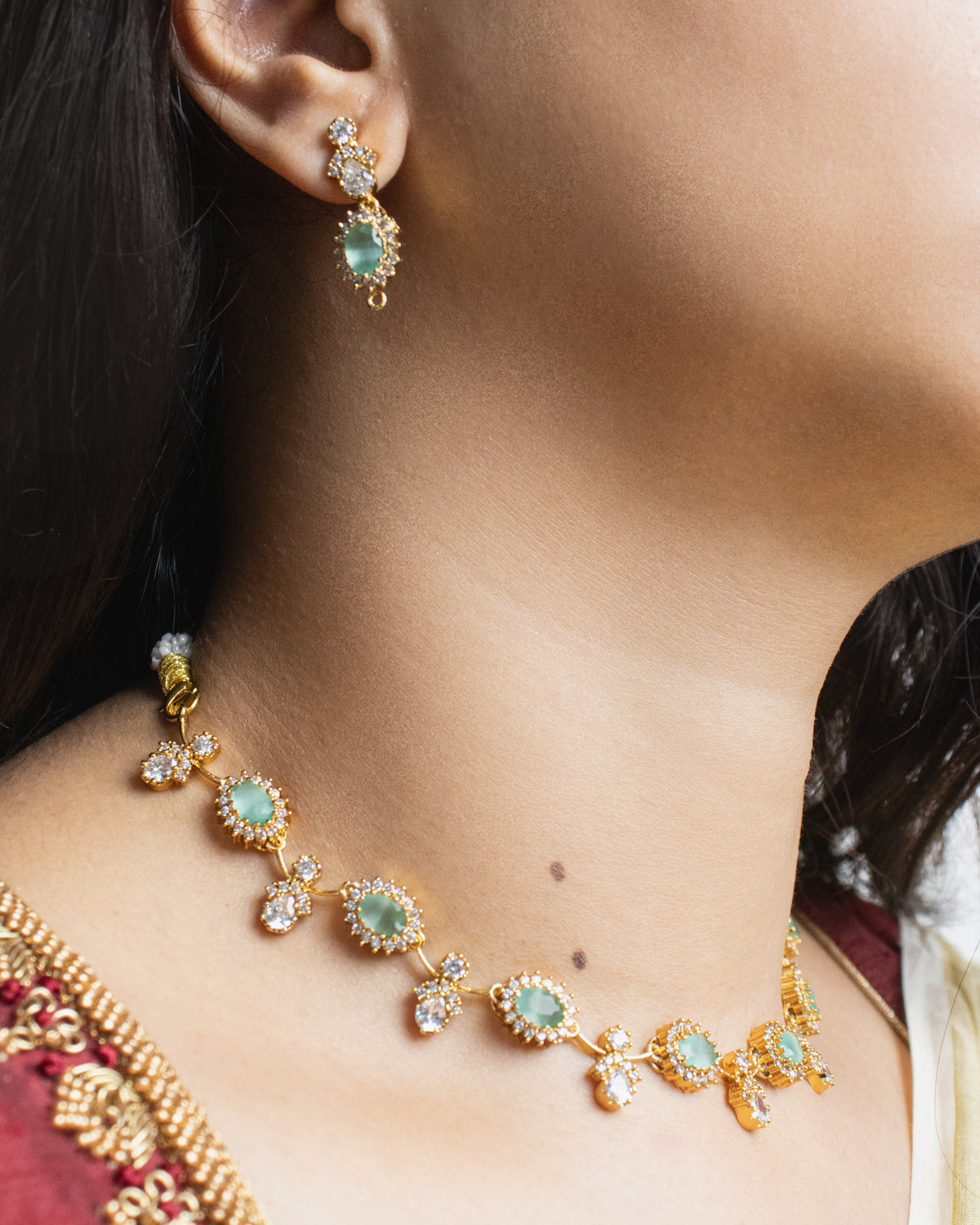 Close-up of a person wearing a gold necklace with green gemstones and matching earrings.