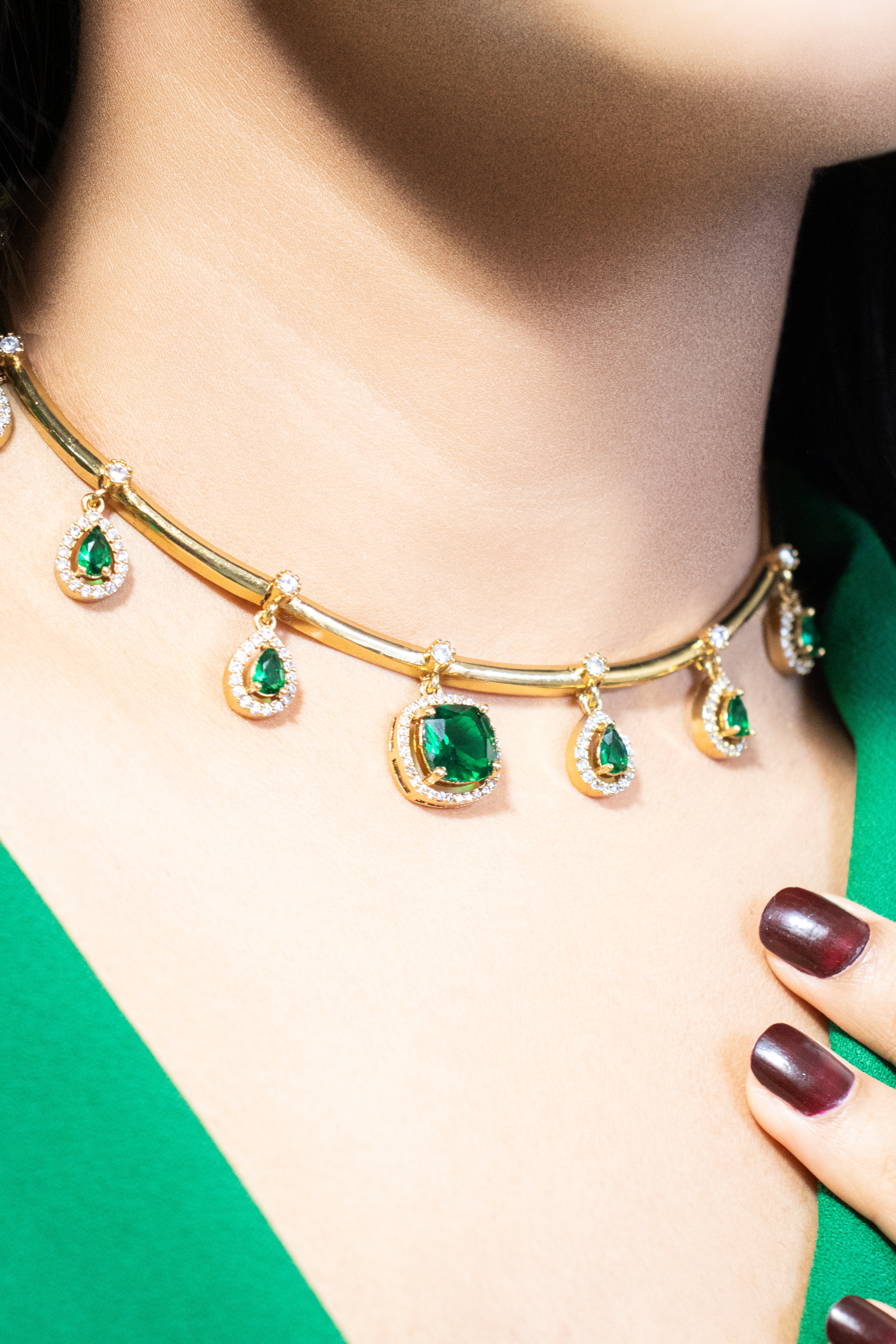 Gold necklace with emerald green gemstones worn by a person against a green background