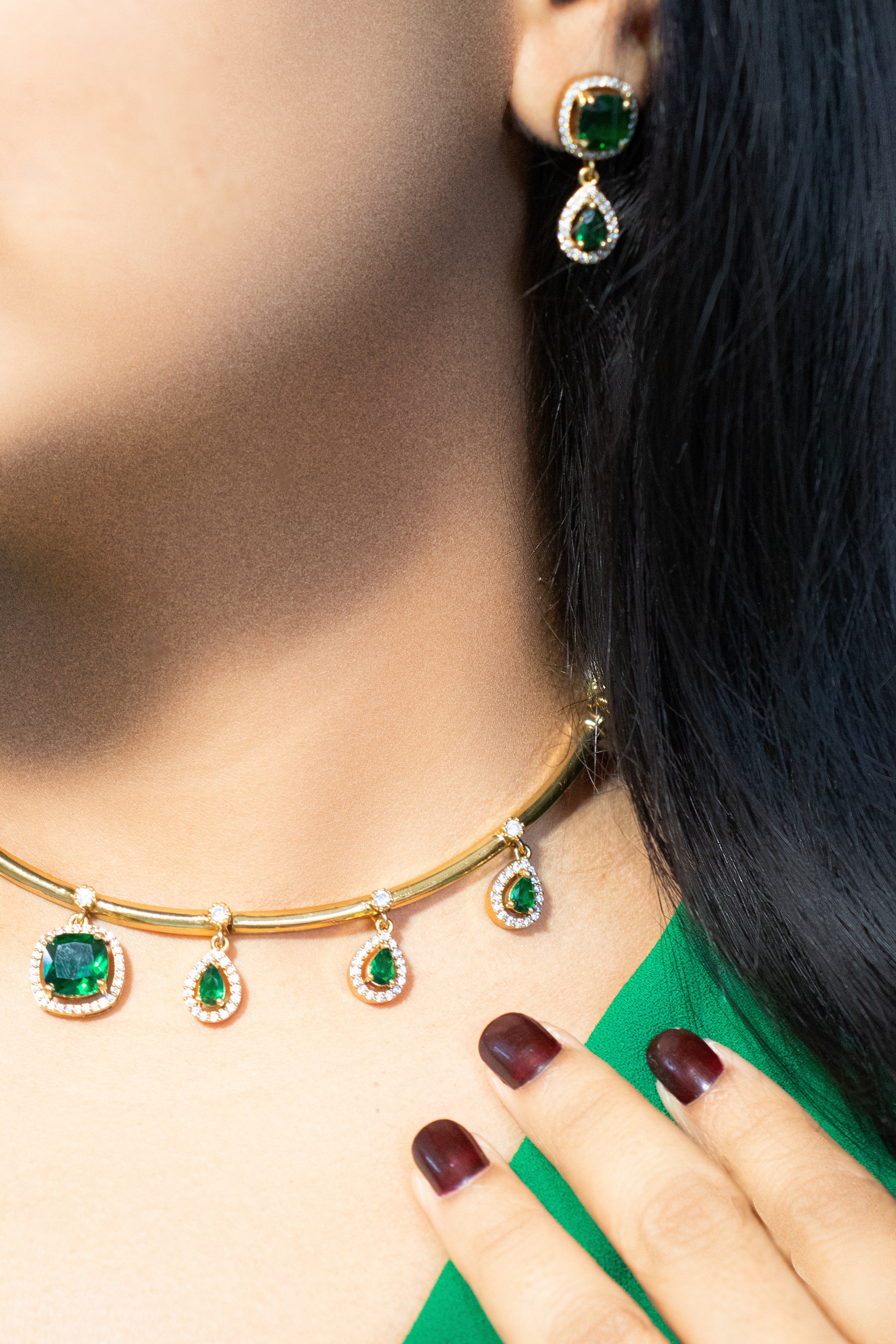 Gold necklace with green gemstones worn by a person, with a close-up of the necklace and hand.