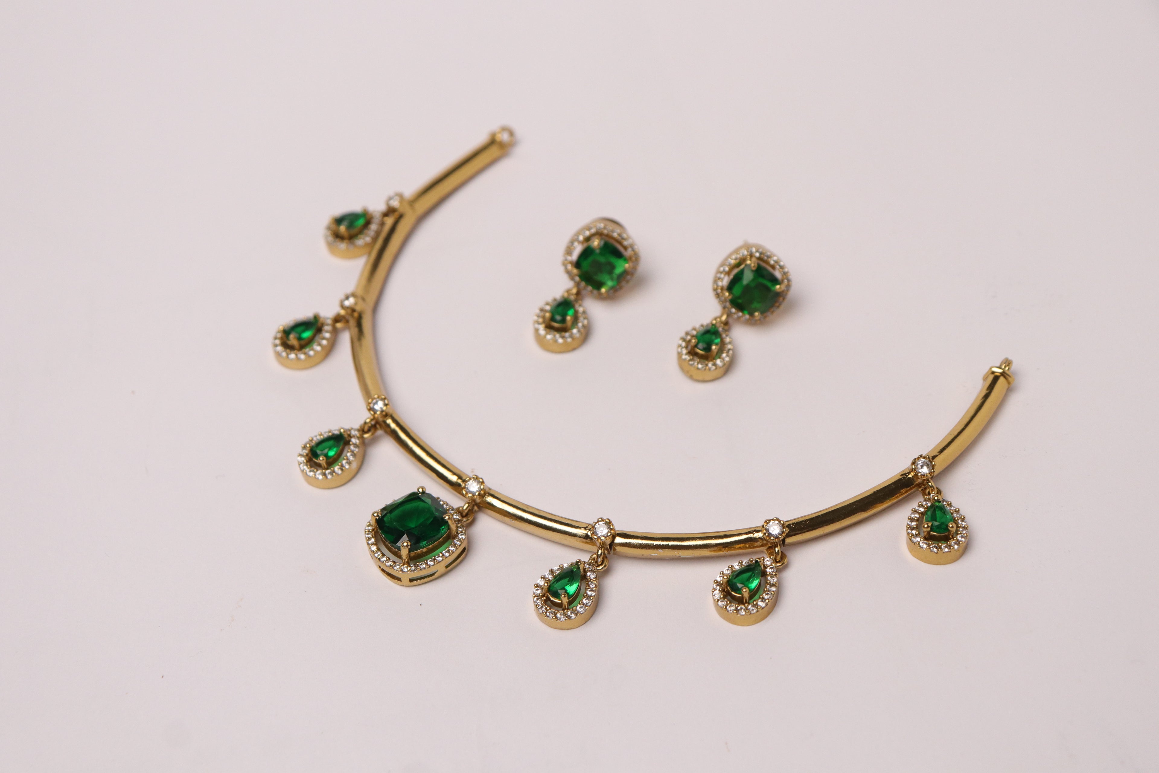 Gold necklace and earrings with green gemstones on a light gray background