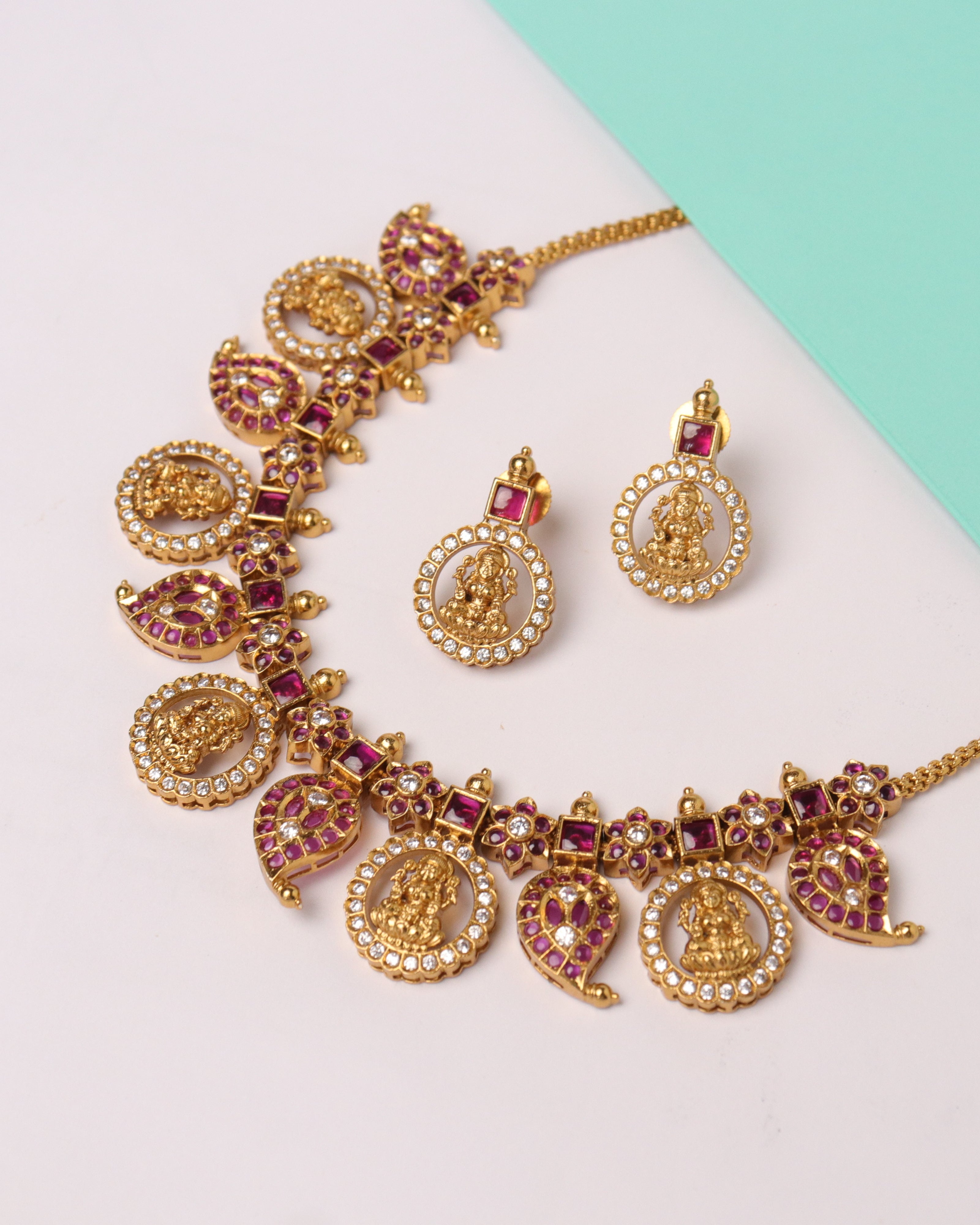 Gold necklace with pink stones and matching earrings on a light background