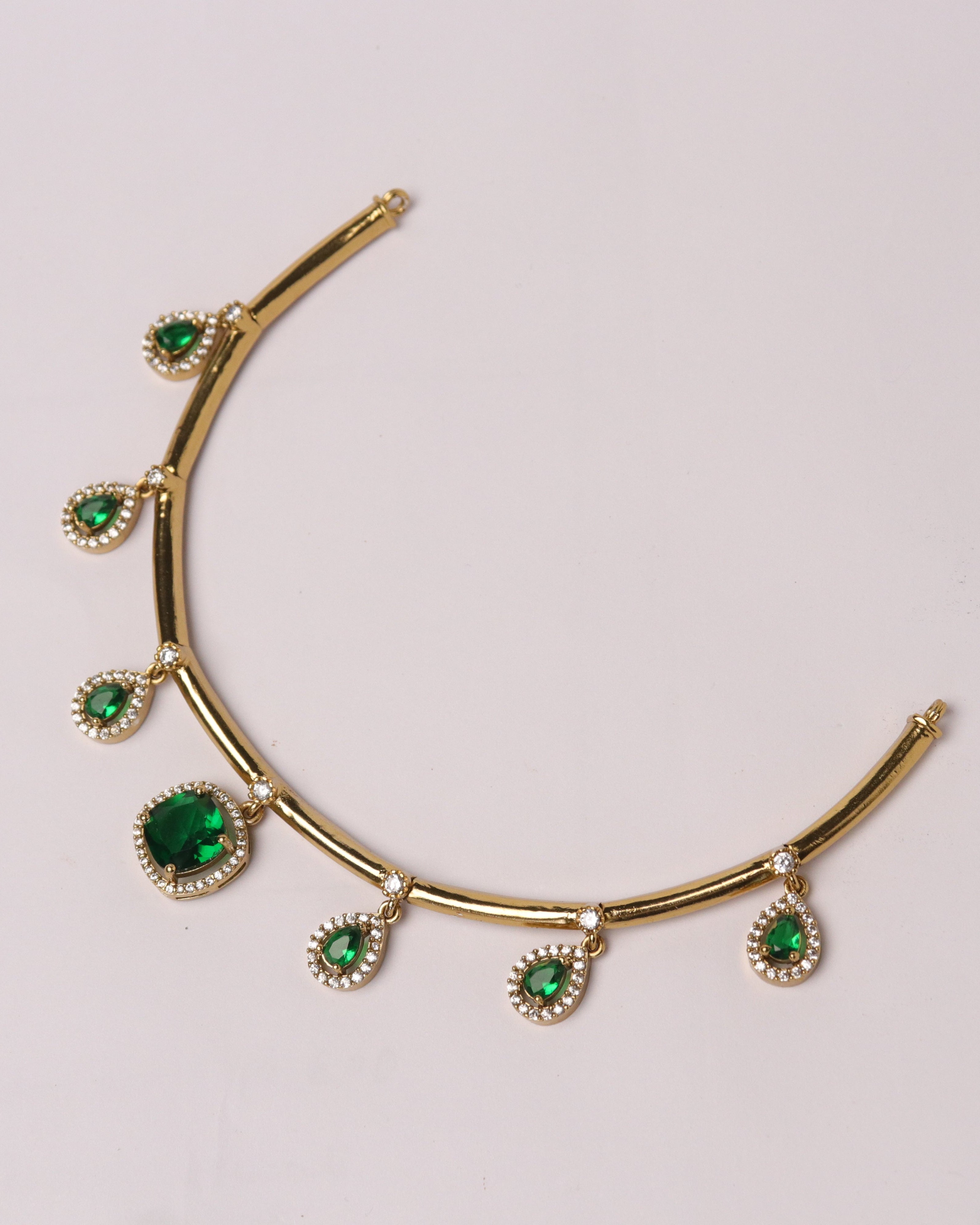 Gold necklace with emerald stones on a light gray background
