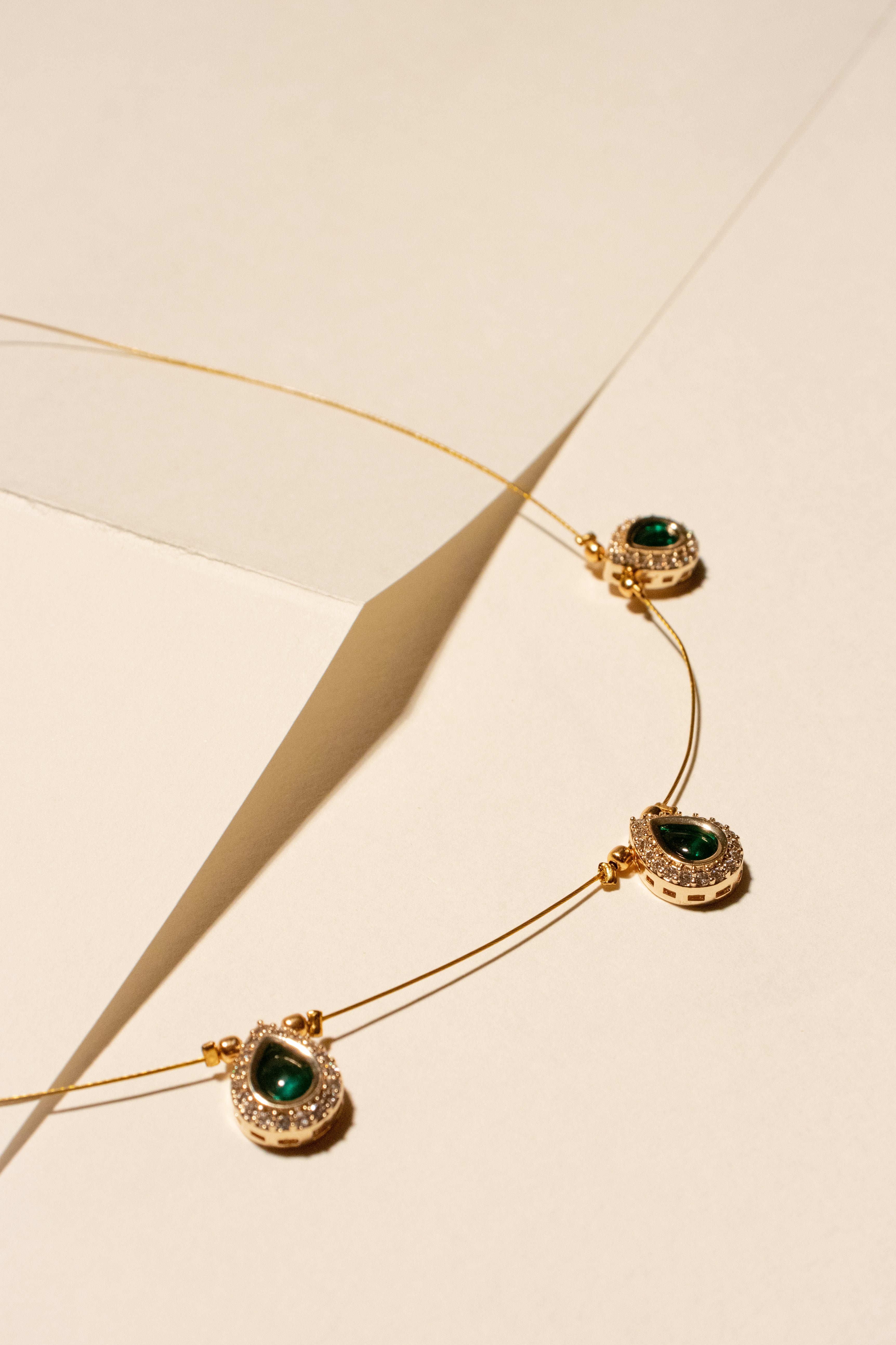 Gold necklace with green gemstones on a beige background