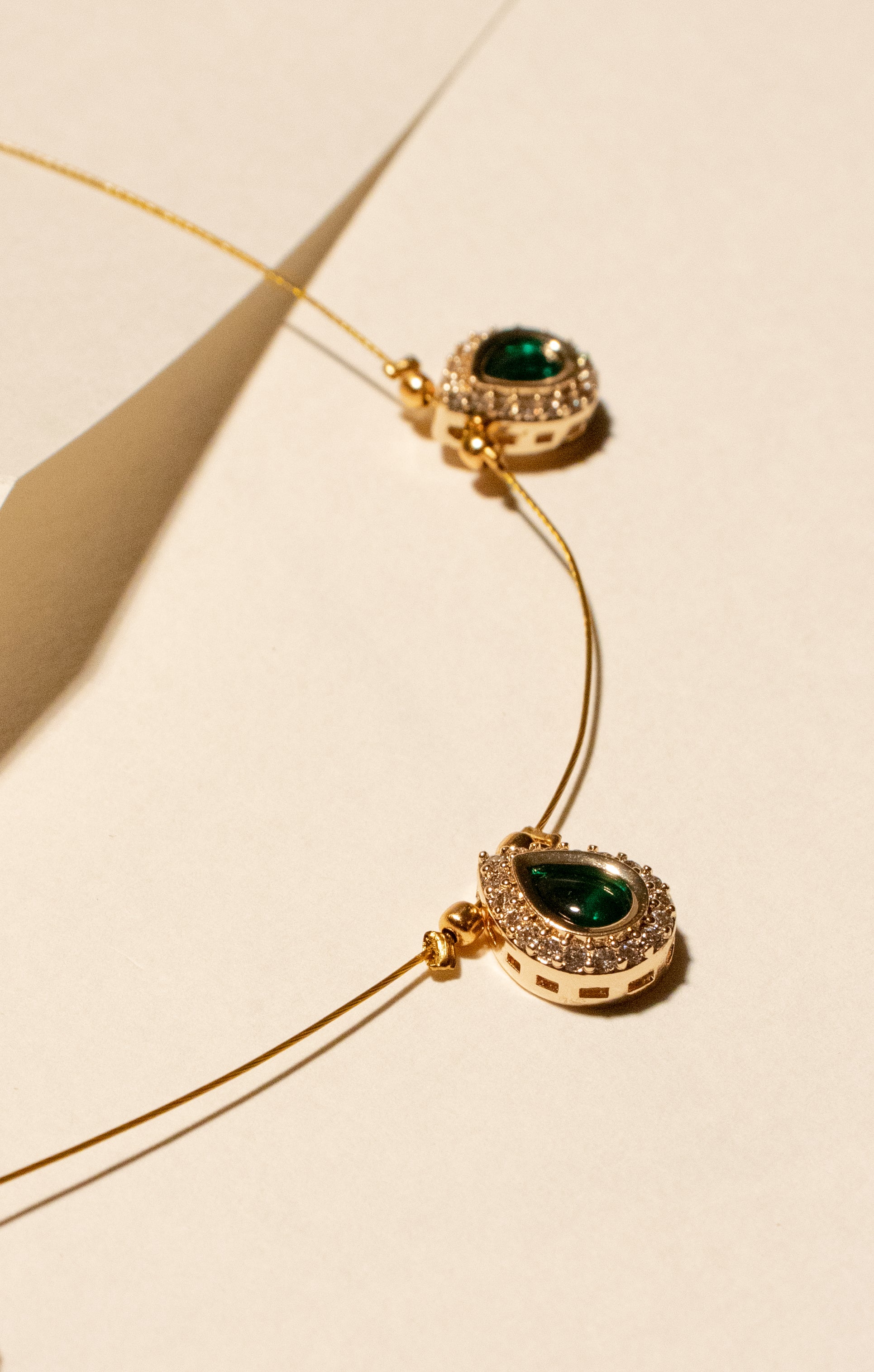 Gold necklace with green gemstones on a beige background
