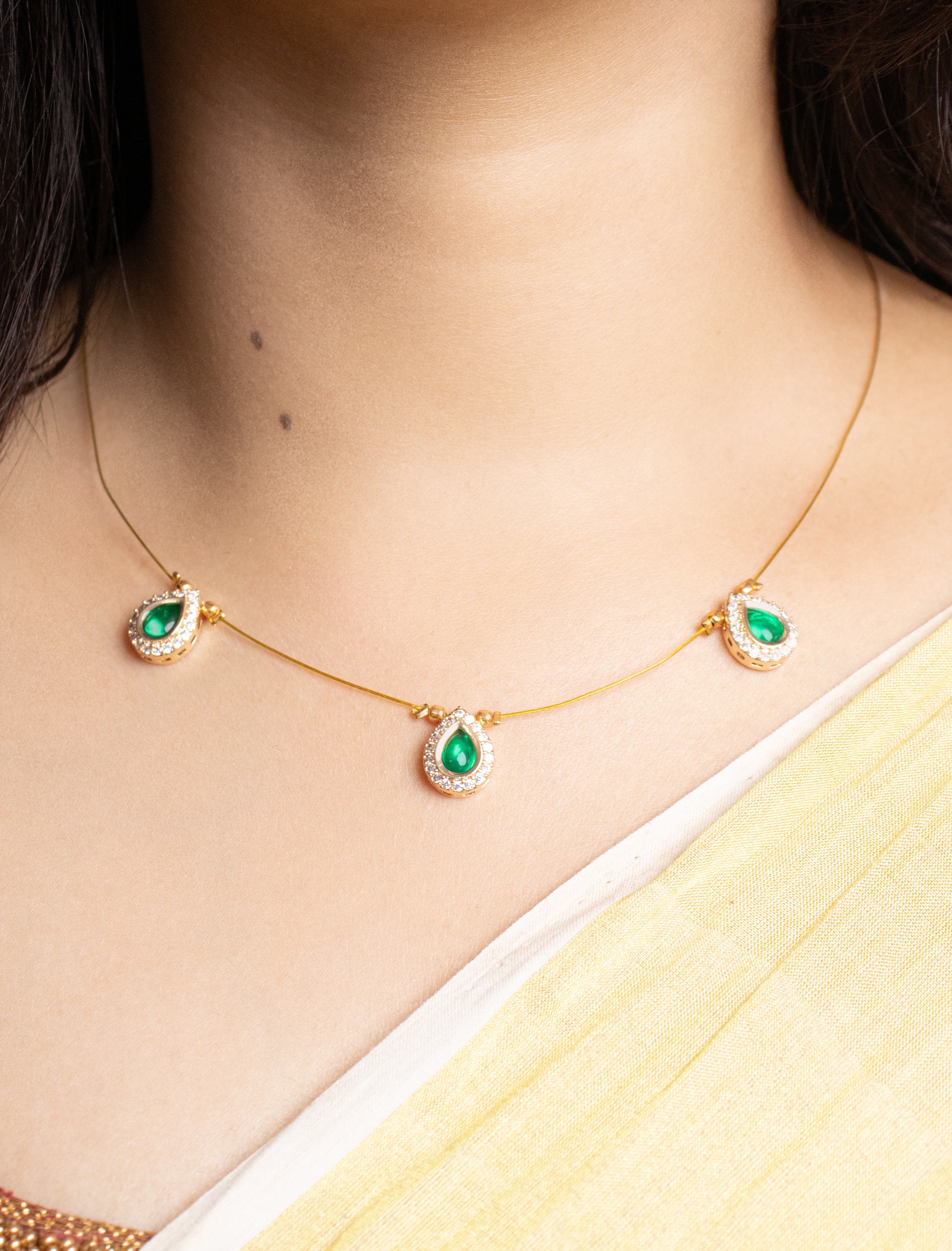 Gold necklace with green gemstones worn by a person, with a blurred background