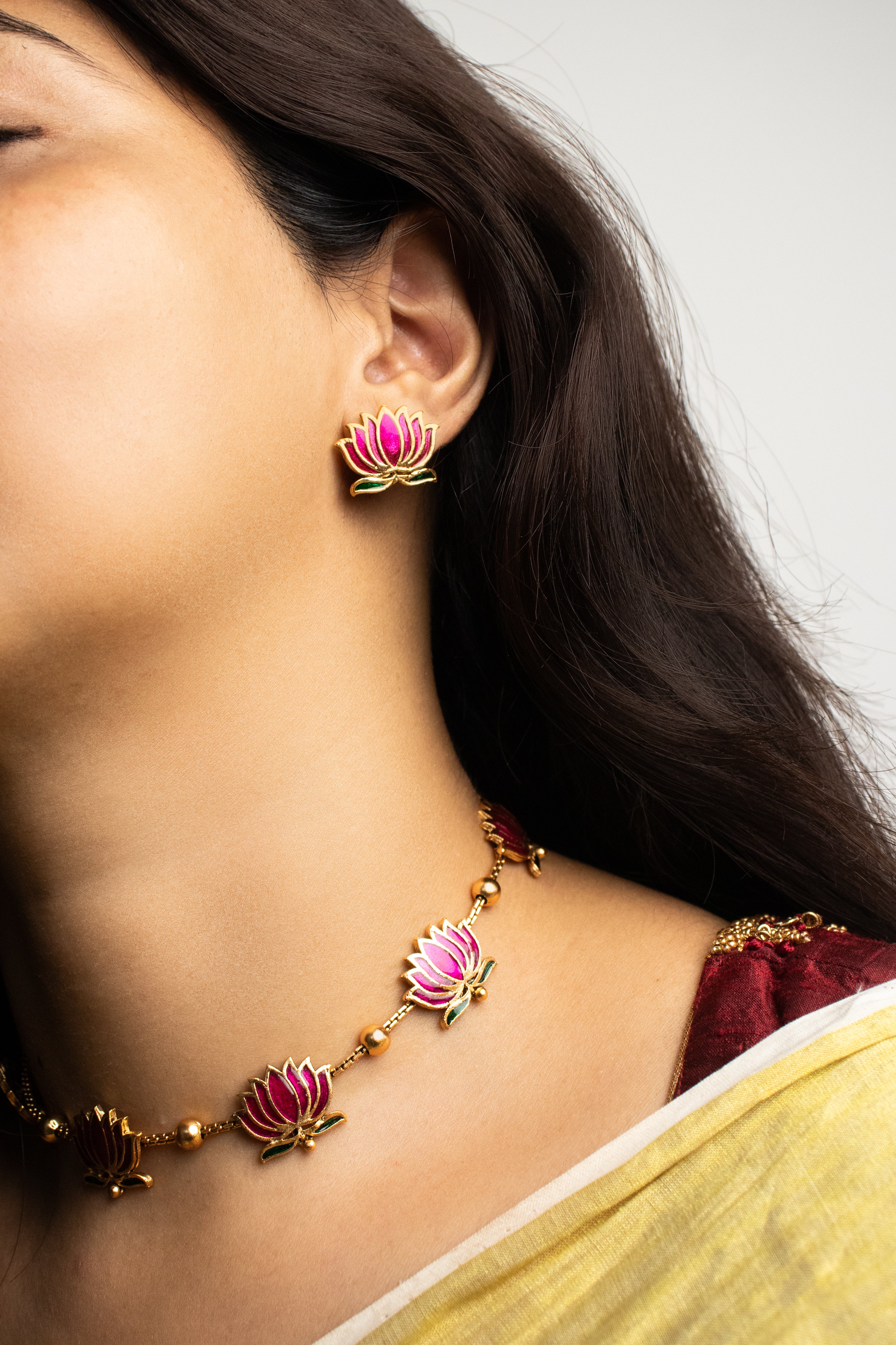 Woman wearing a gold necklace and earrings with pink floral designs.