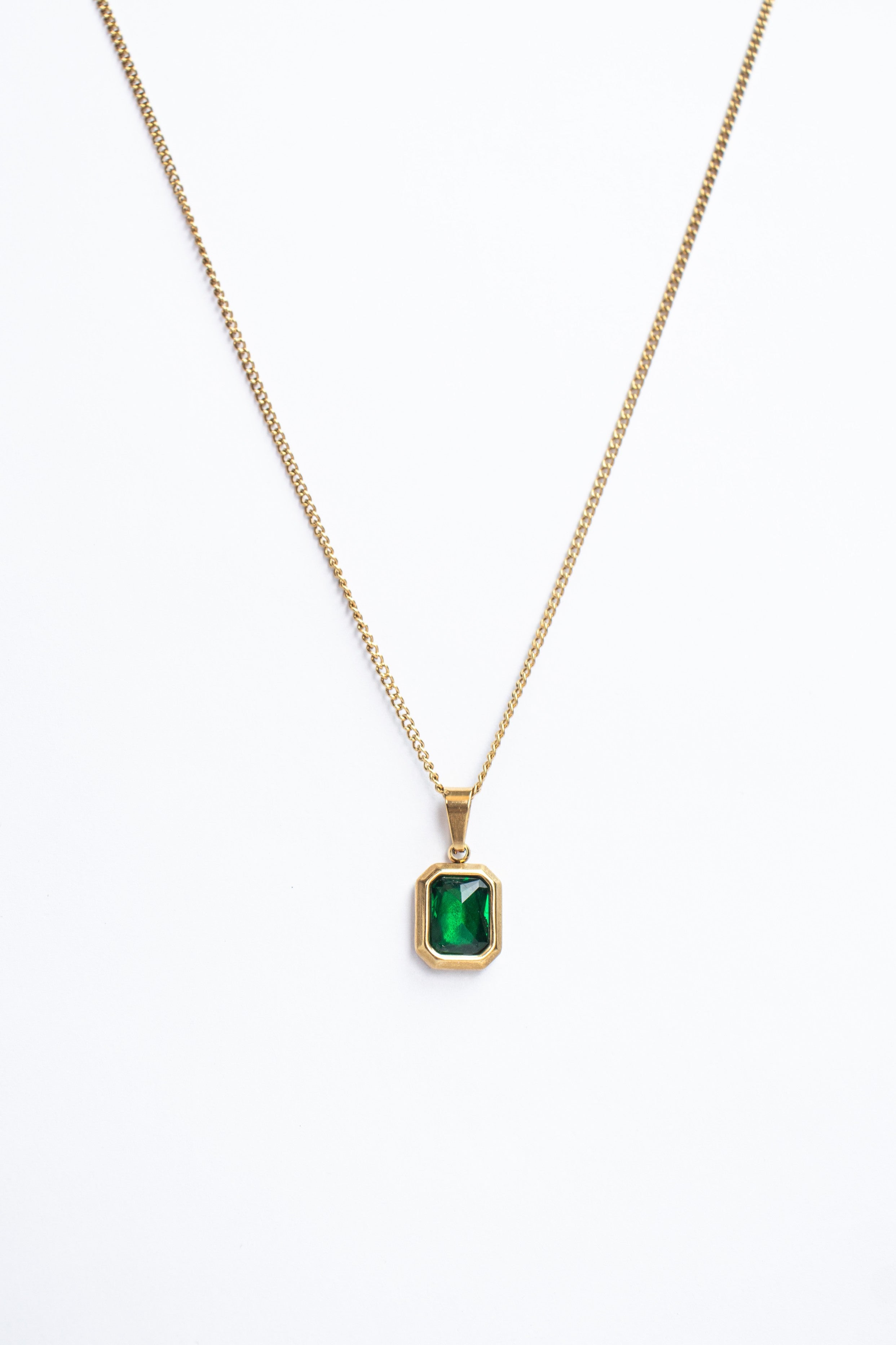 Gold necklace with a green gemstone pendant on a white background
