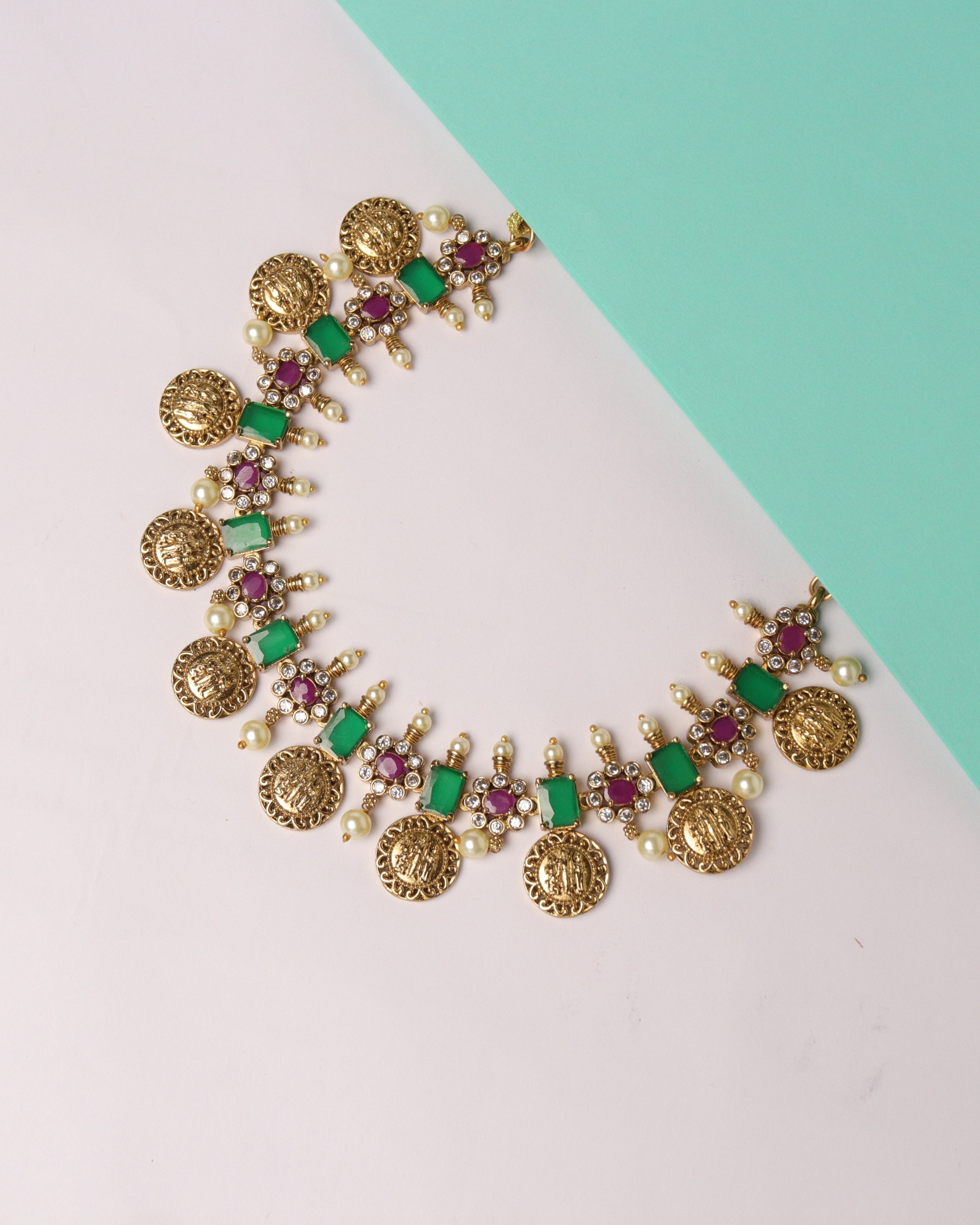 Decorative gold necklace with green and red gemstones on a two-tone background