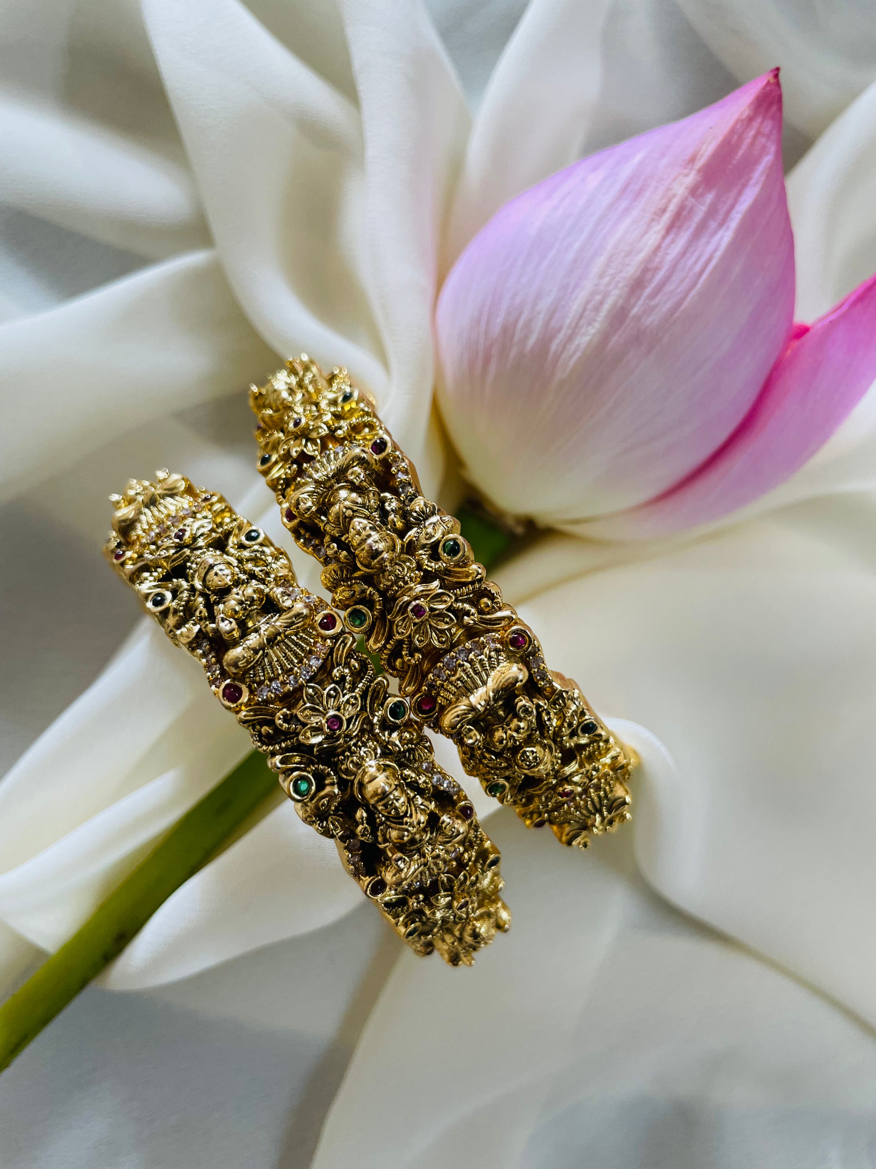 Gold bangles with intricate designs on a white flower background