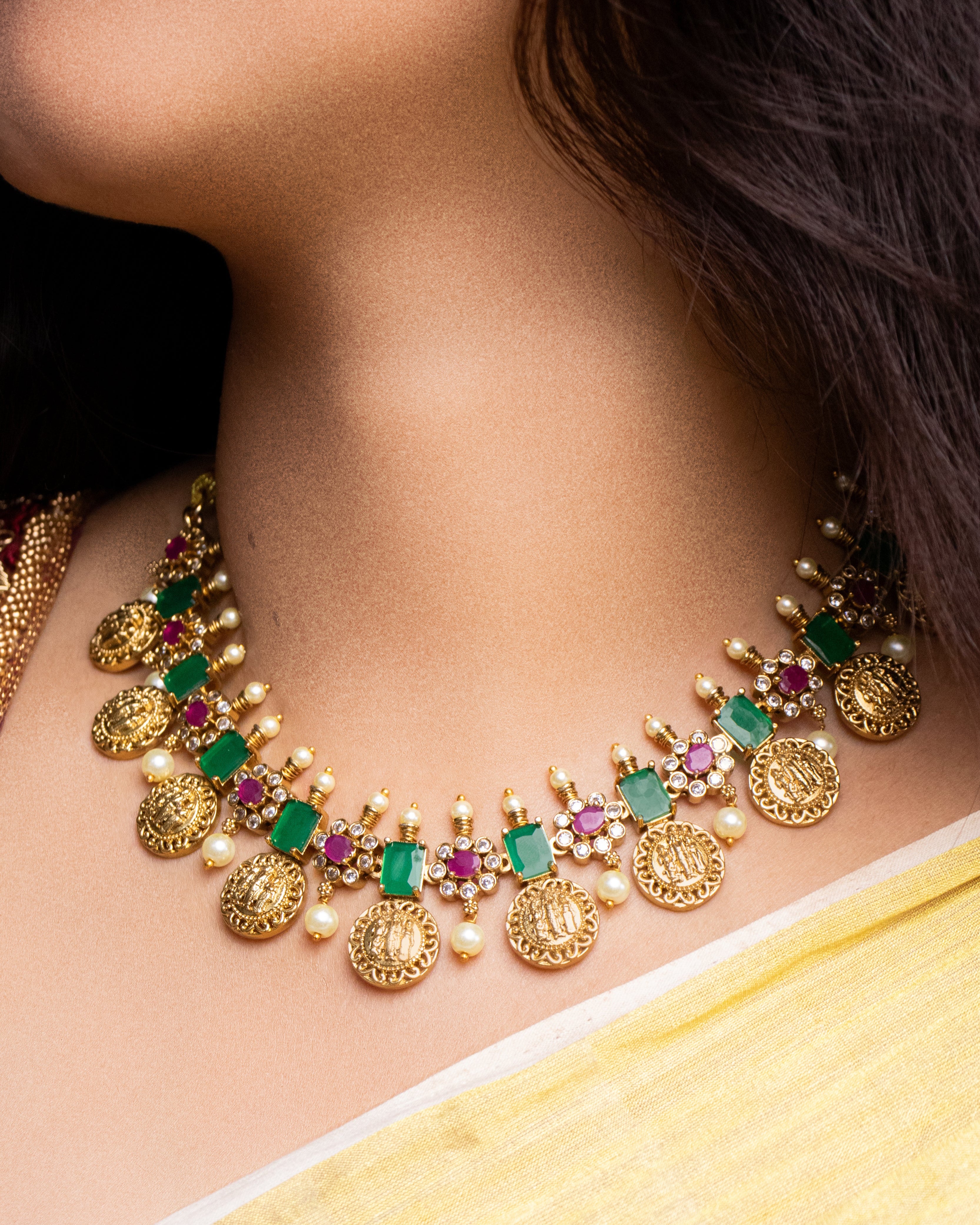 Gold necklace with emeralds and rubies on a person wearing a yellow saree.