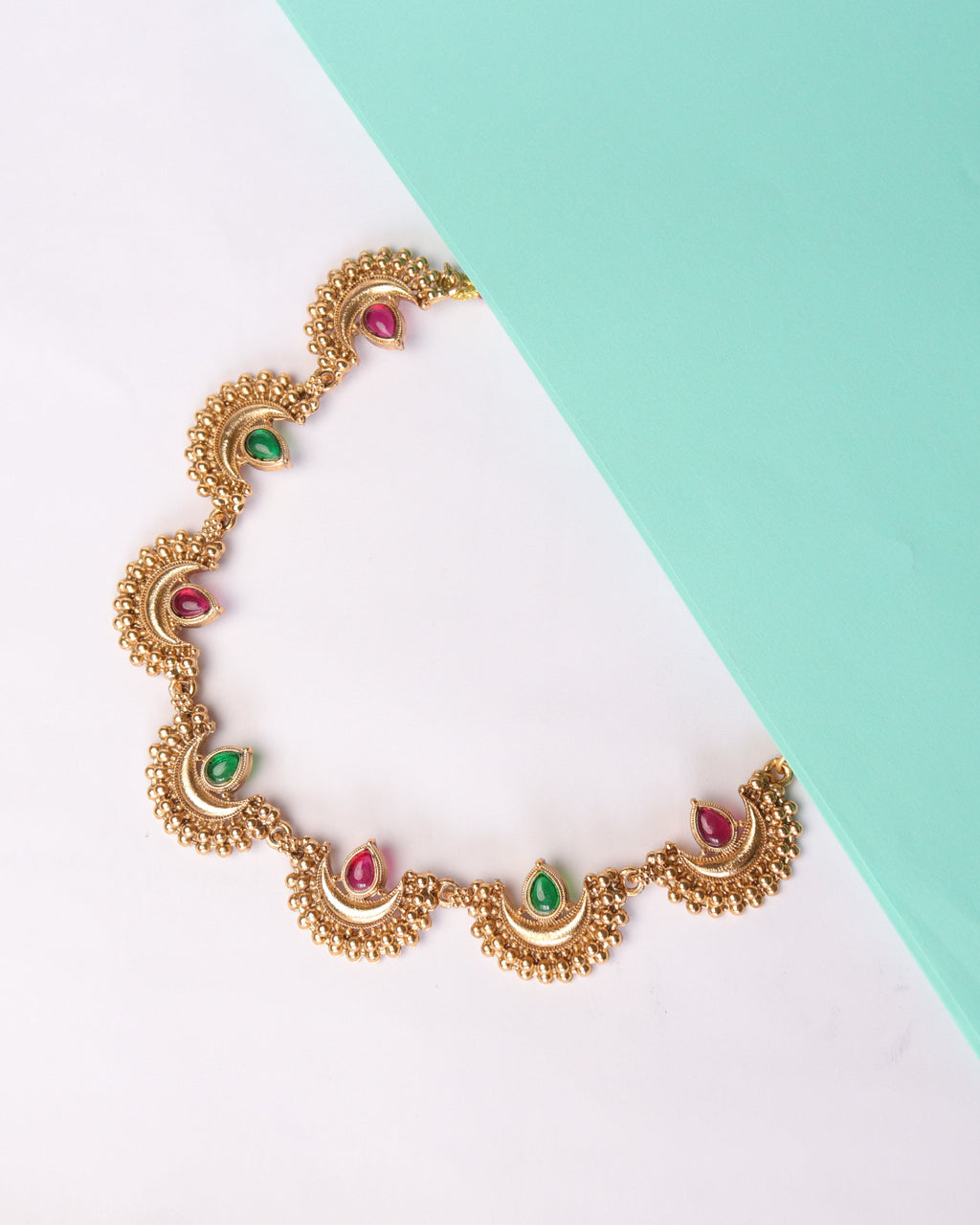 Gold necklace with colorful stones on a white and light blue background