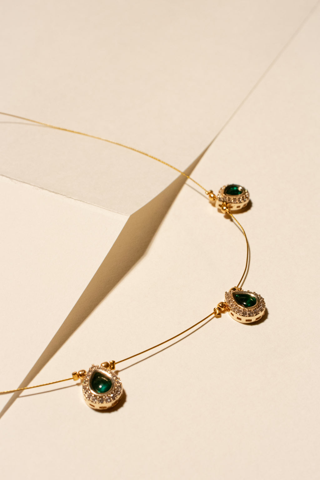 Gold necklace with green gemstones on a beige background