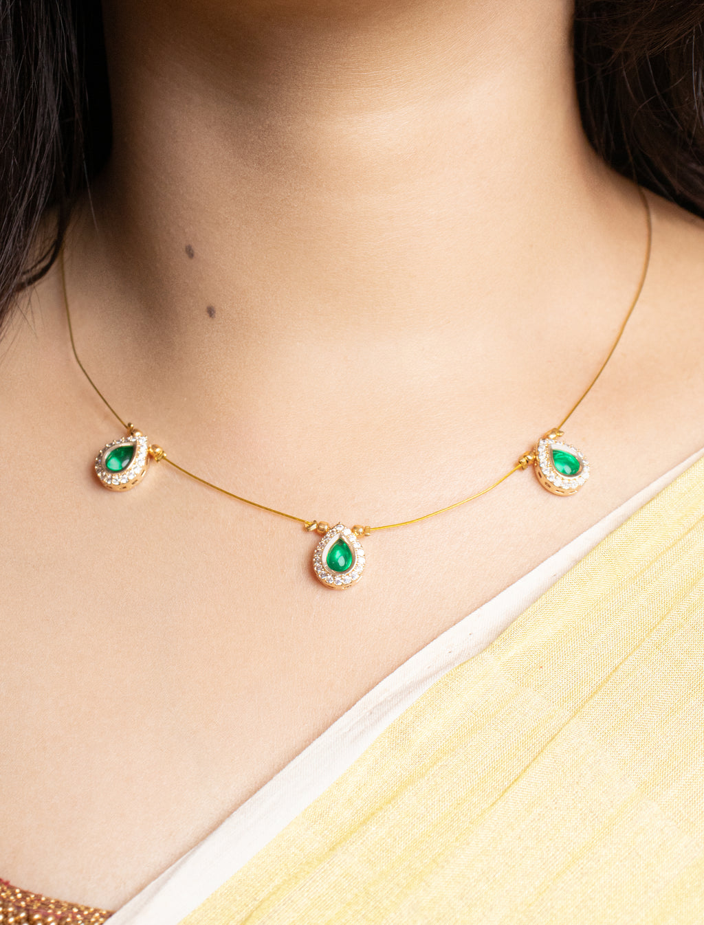 Gold necklace with green gemstones worn by a person, with a blurred background