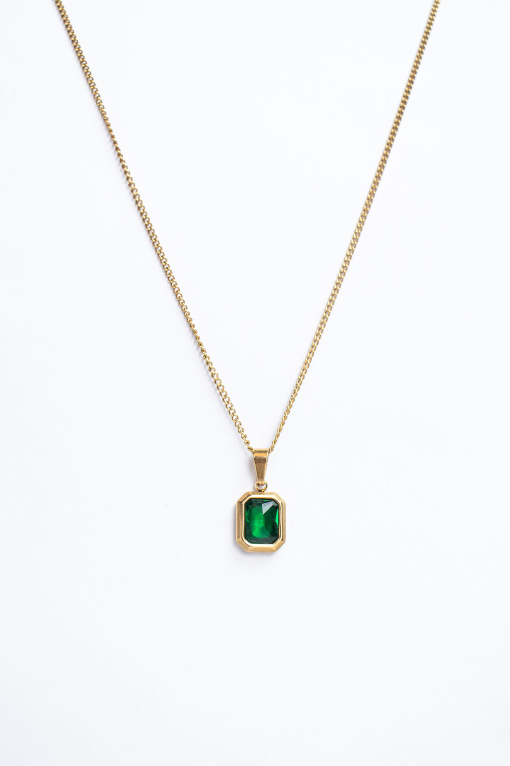 Gold necklace with a green gemstone pendant on a white background