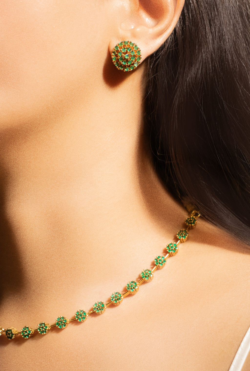 Close-up of a person wearing green gemstone earrings and a matching necklace.