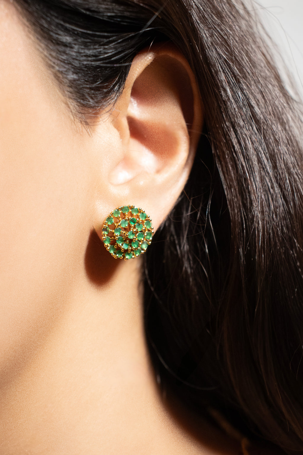 Close-up of an ear wearing a green and gold stud earring with dark hair.