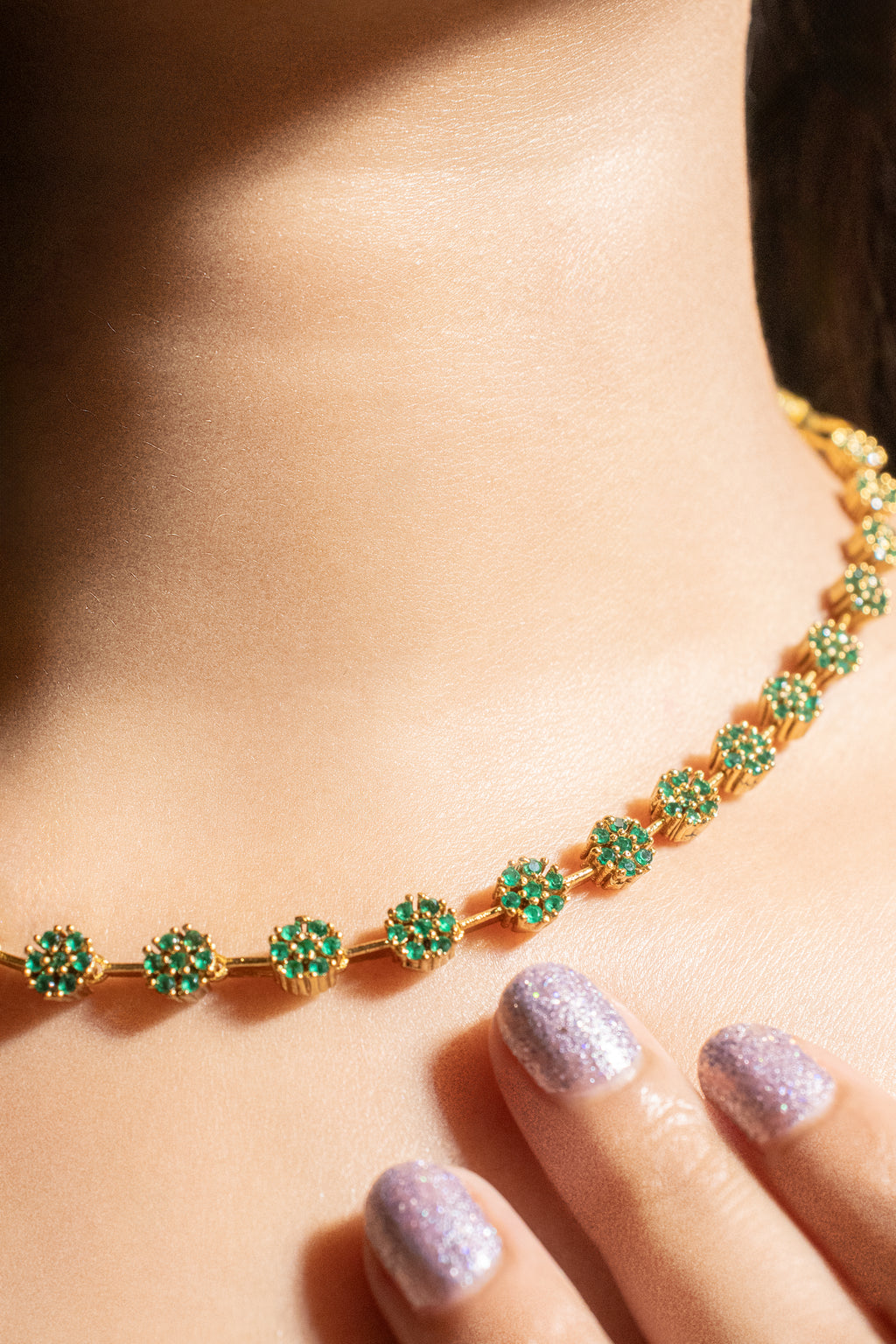 Gold necklace with green gemstones worn by a person, focusing on the jewelry.